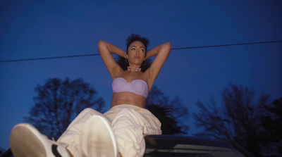 a woman in a bra top and white pants sitting on top of a car