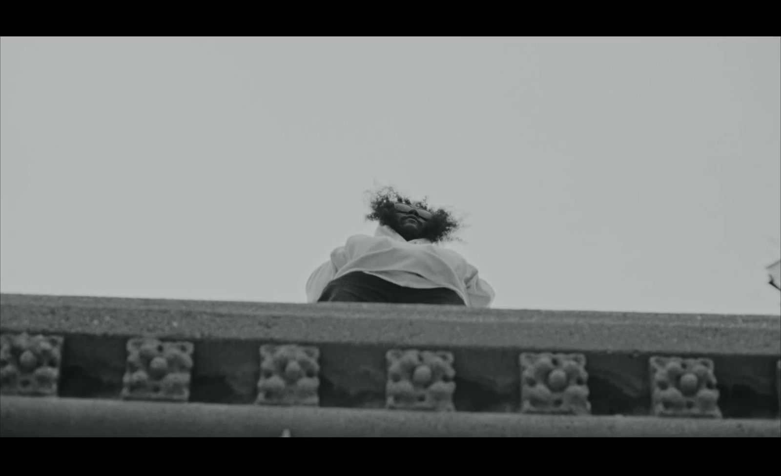 a black and white photo of a person looking over a wall