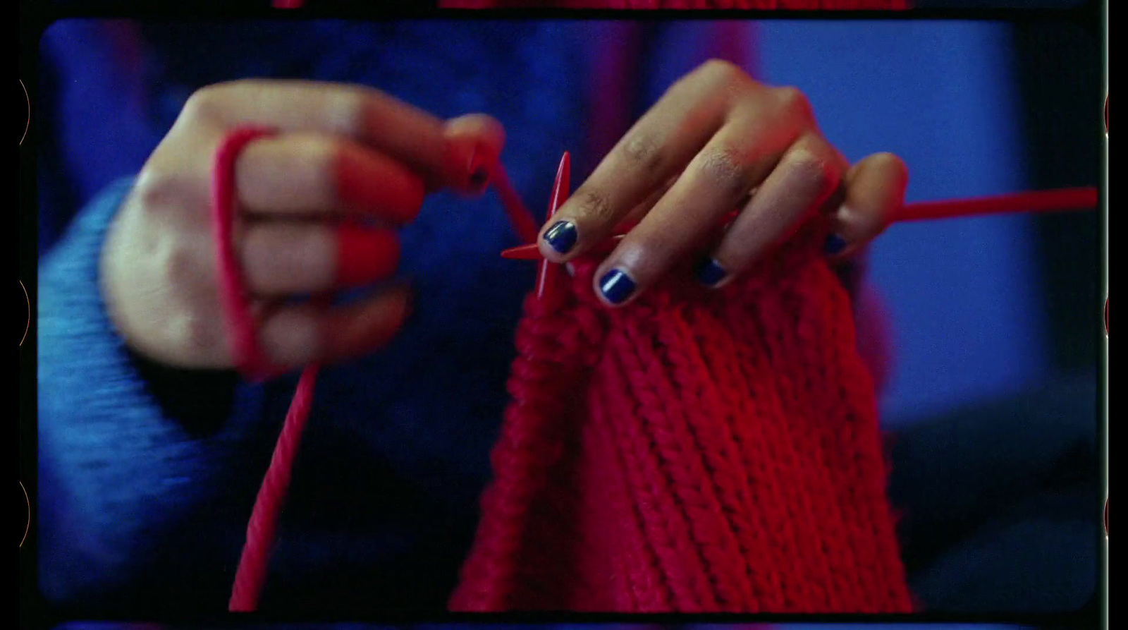 a woman is knitting a red piece of yarn