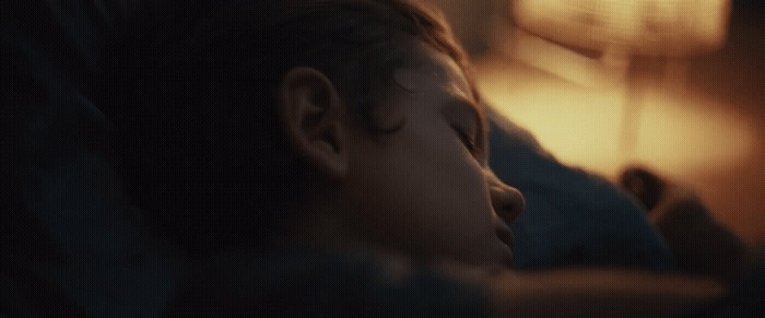 a young boy sleeping on a bed next to a lamp