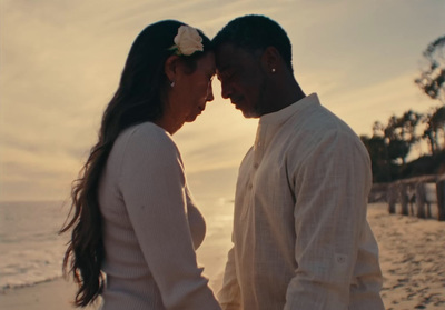 a man and woman standing on a beach next to the ocean