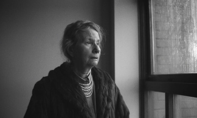 a black and white photo of a woman looking out a window