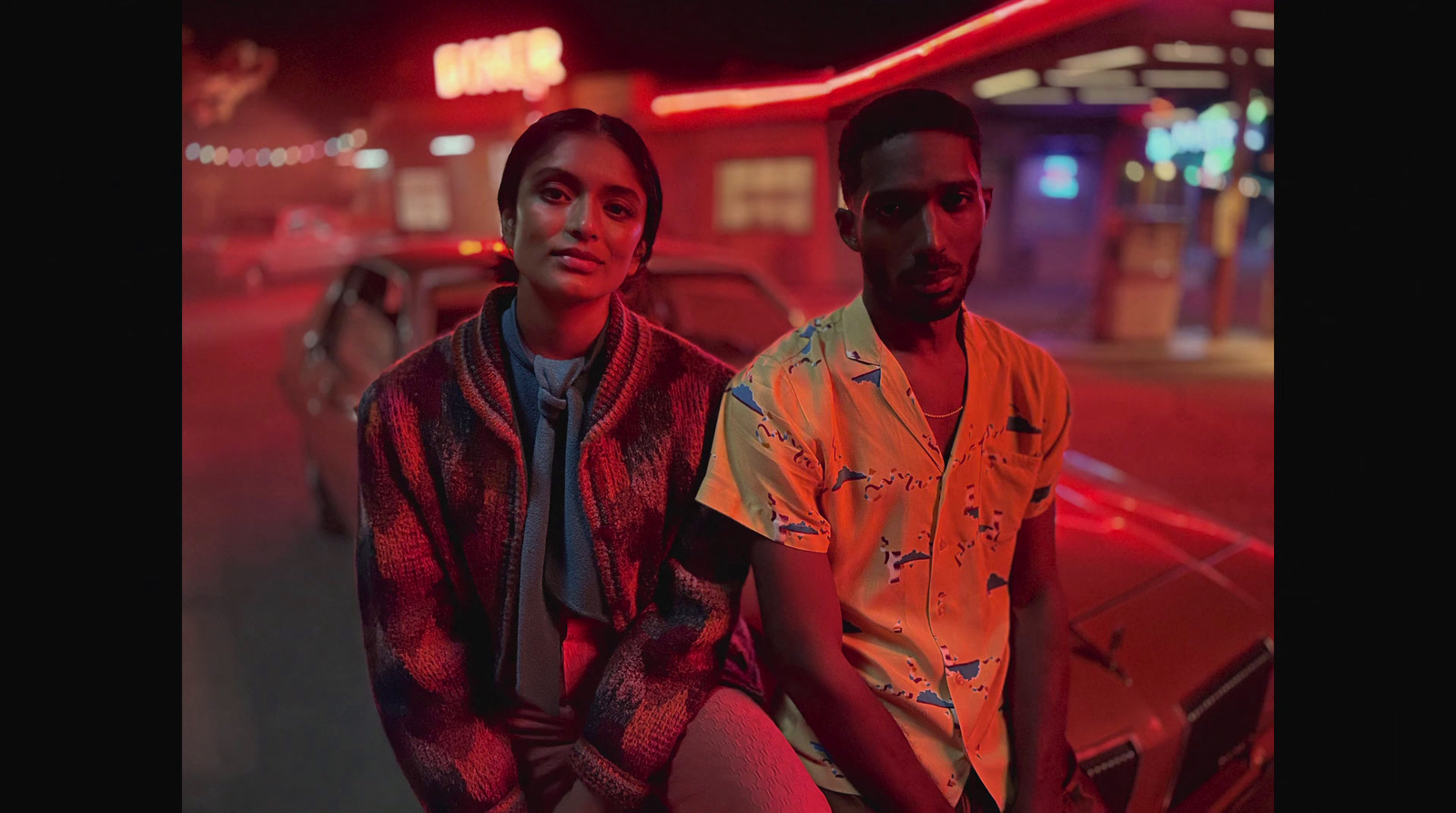 two men sitting on a car at night