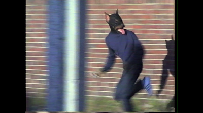 a man in a cat mask walking by a brick wall