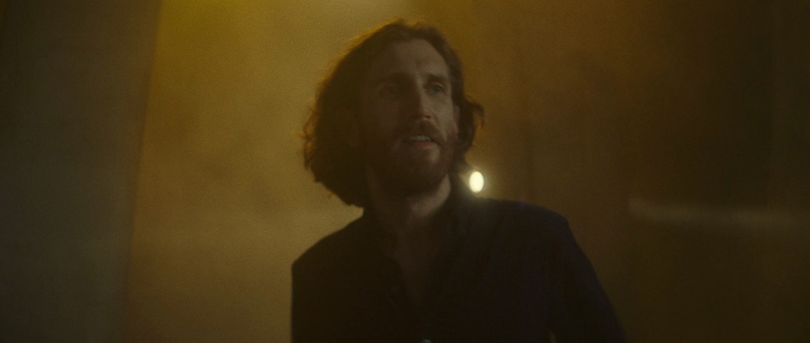 a man with long hair and beard standing in a dimly lit room