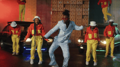 a man in a white suit and yellow pants dancing in front of a group of