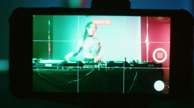 a person taking a picture of a dj on a video screen