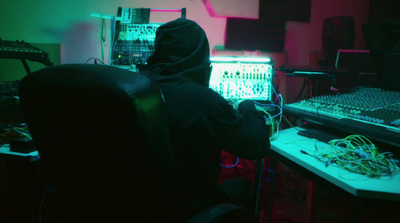 a person in a hoodie sitting in front of a mixing desk